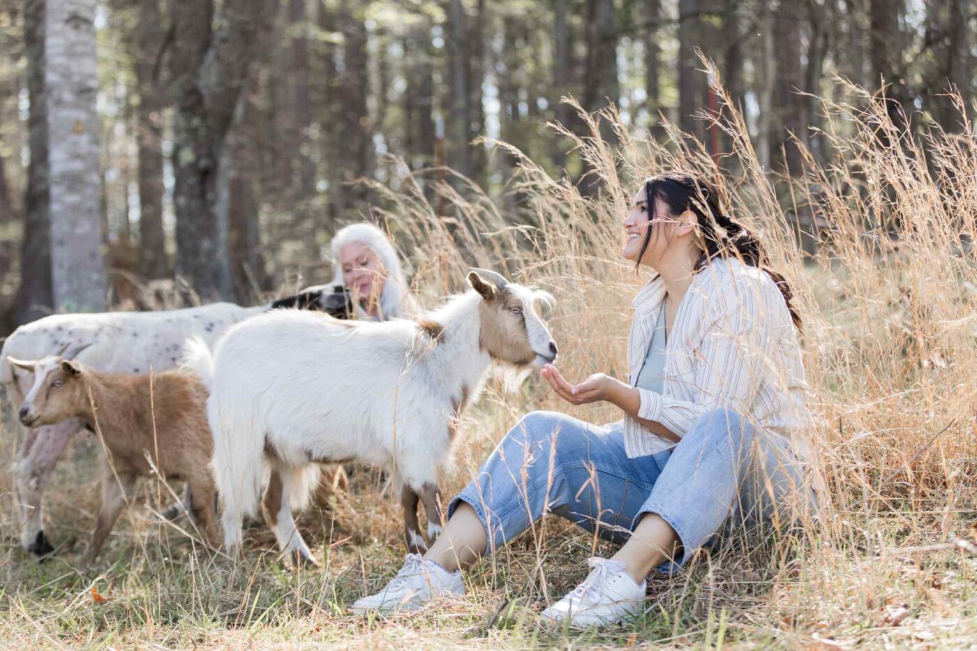 two women sitting on the ground playing with goats