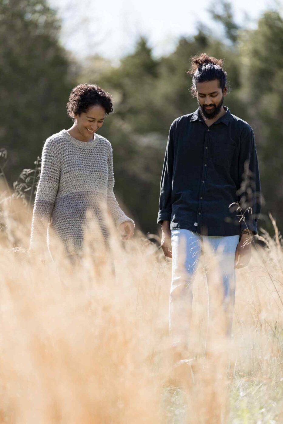 two people walking through a field of tall grass