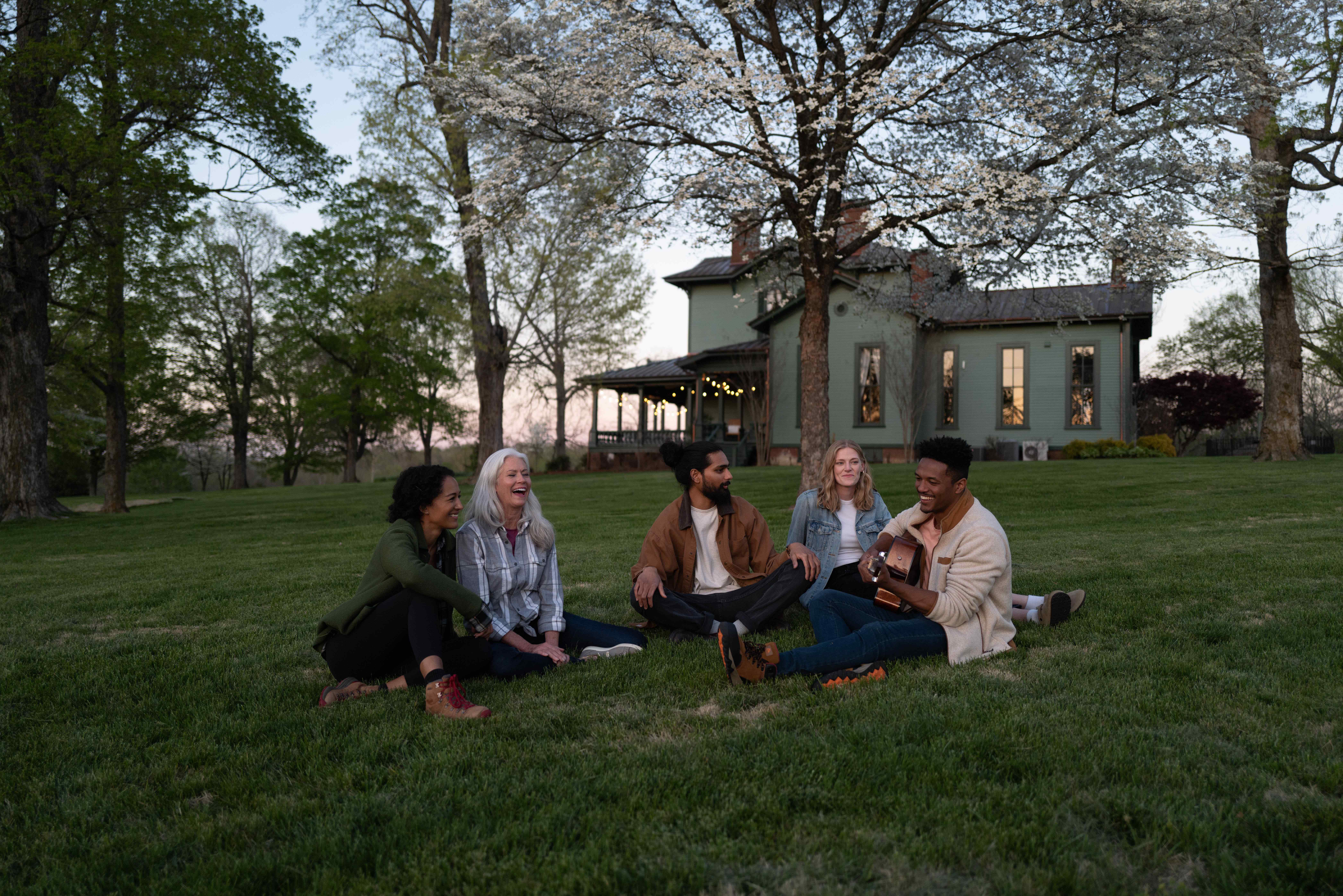 group of people sitting on the grass outside of a large green house