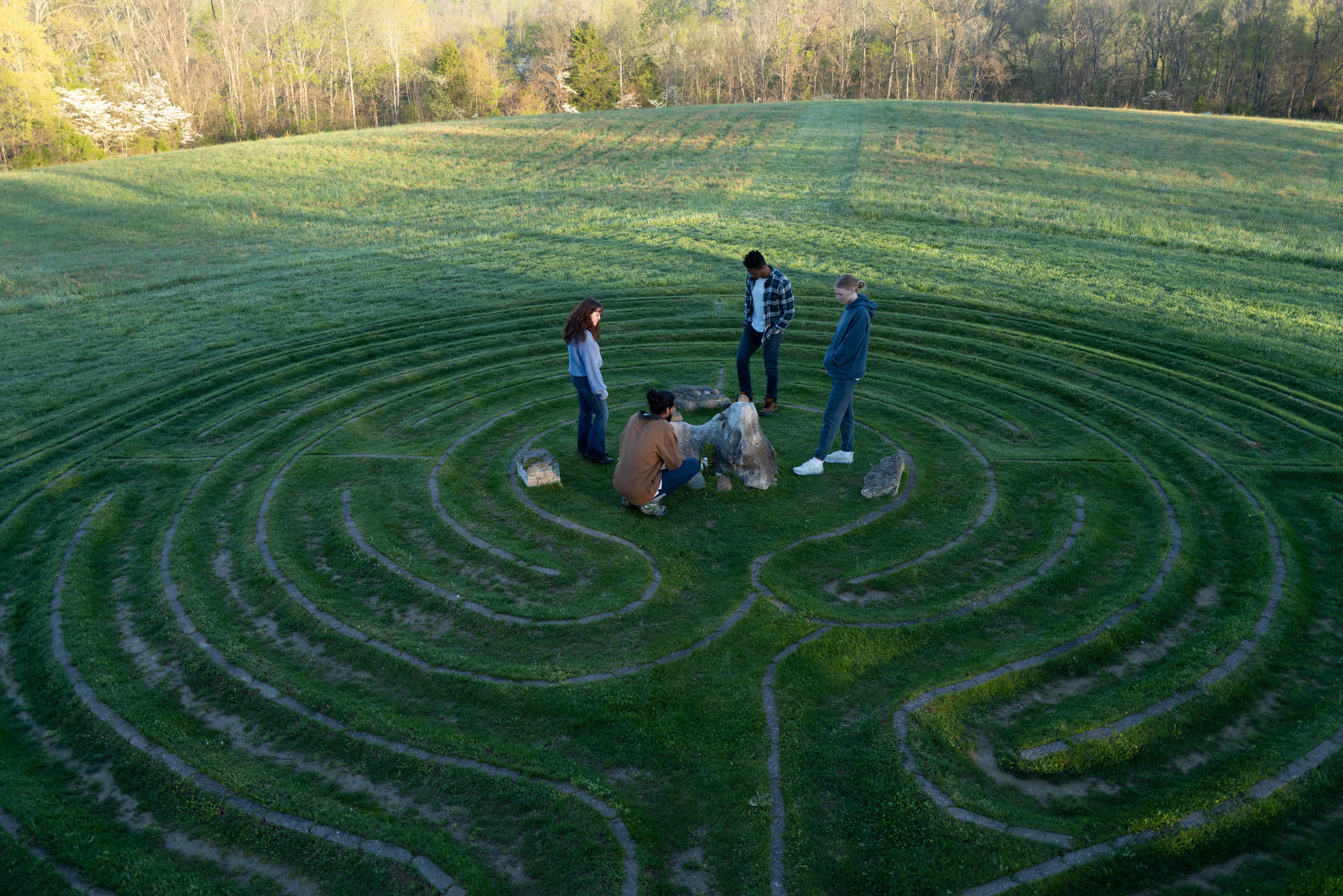 group of people standing and sitting in the middle of a grassy labyrinth path