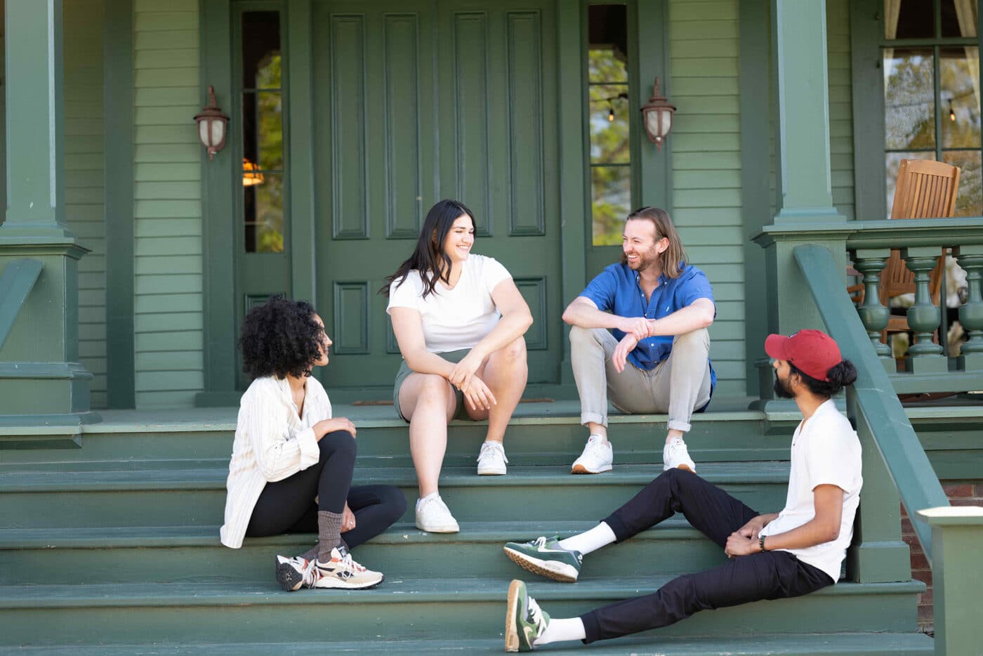 group of people sitting and chatting on the steps of a green house