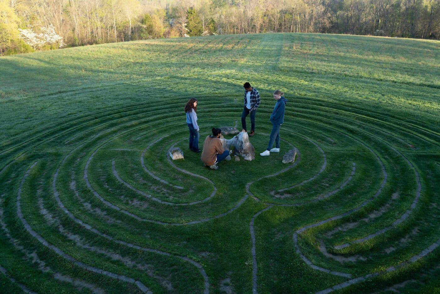 group of people standing and sitting in the middle of a grassy labyrinth path