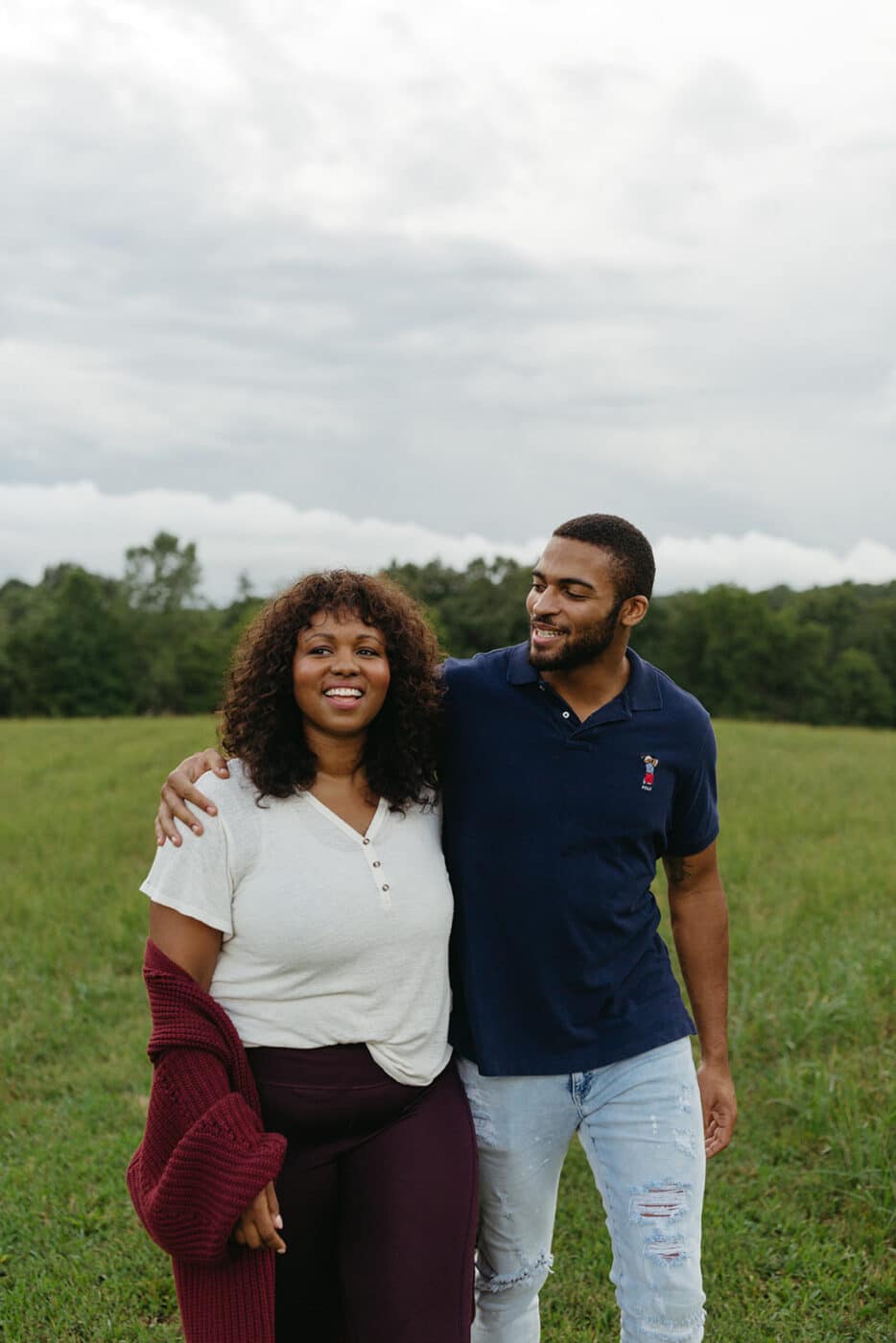 Two people hugging sideways while standing in a grassy field