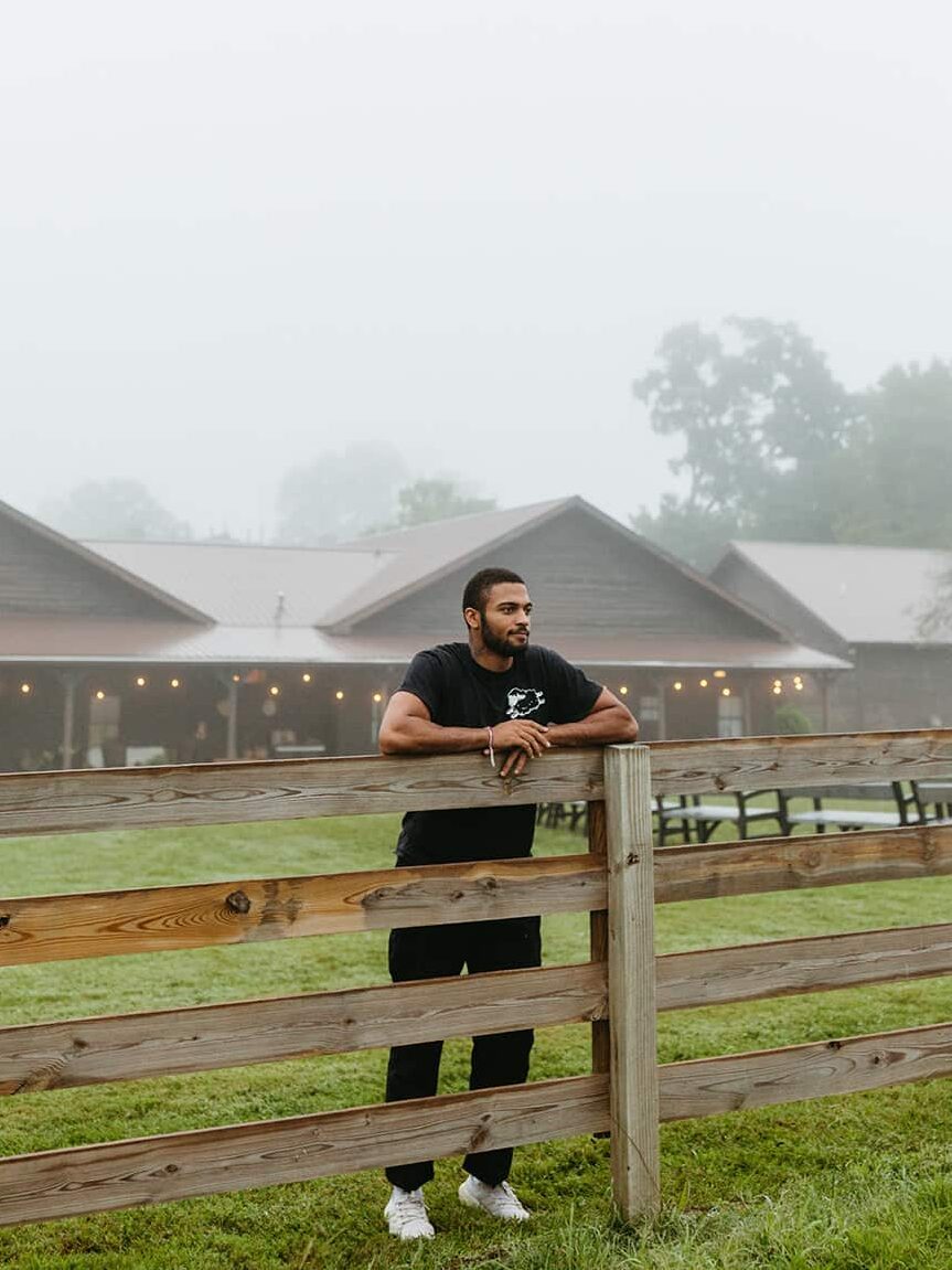 A man stands against a fence, looking into the distance