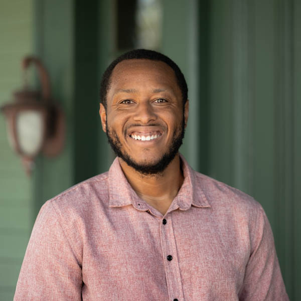 Onsite team member portrait, smiling man in button-down shirt, emotional wellness advocate.